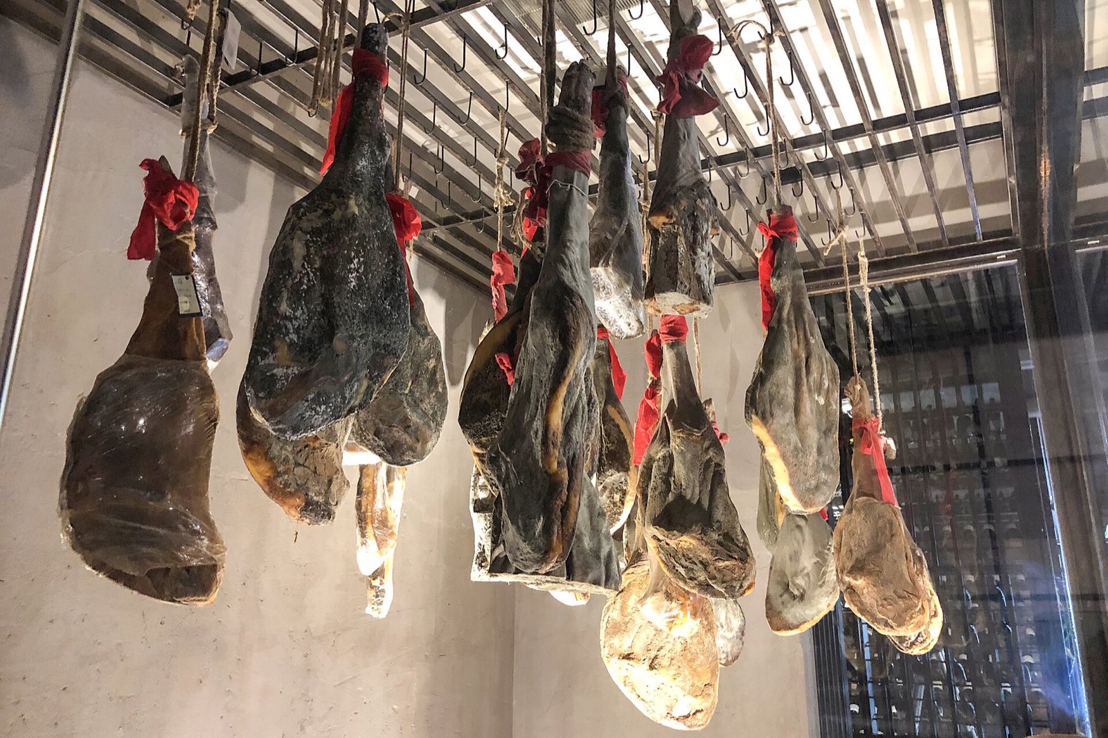 风干房里的宣威火腿：整条火腿系着麻绳挂在金属挂钩上，表皮深褐油润，一排排等着时间
